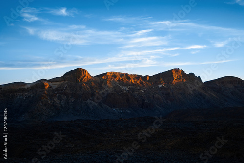 Beautiful colorful sunset over the rocky mountain range surrounded by dry wasteland. Nature landscape. Blue sky with white clouds.