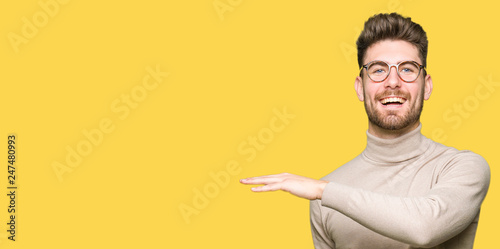Young handsome business man wearing glasses gesturing with hands showing big and large size sign, measure symbol. Smiling looking at the camera. Measuring concept.