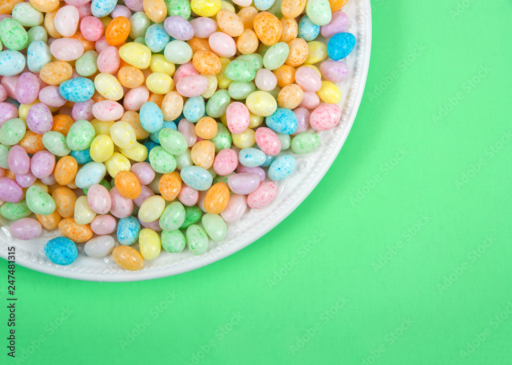 Many colorful candy jelly beans on porcelain plate laying on light green surface with copy space. Popular Easter candy.