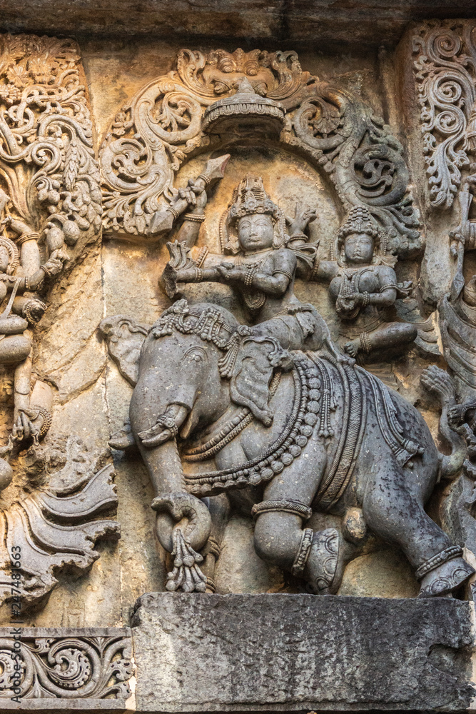 Halebidu, Karnataka, India - November 2, 2013: Hoysaleswara Temple of Shiva. Closeup of statue on side of main sanctuary, where Lord Shiva and Devi Parvati sit on elephant. Gray stone with brown back.