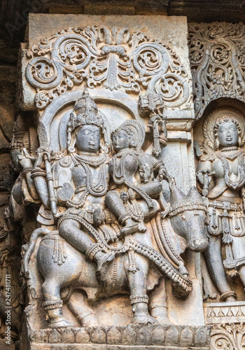 Halebidu, Karnataka, India - November 2, 2013: Hoysaleswara Temple of Shiva. Statue on side of main sanctuary, where Lord Shiva and Devi Parvati sit Nandi Bull. Other figures around. Gray stone with b