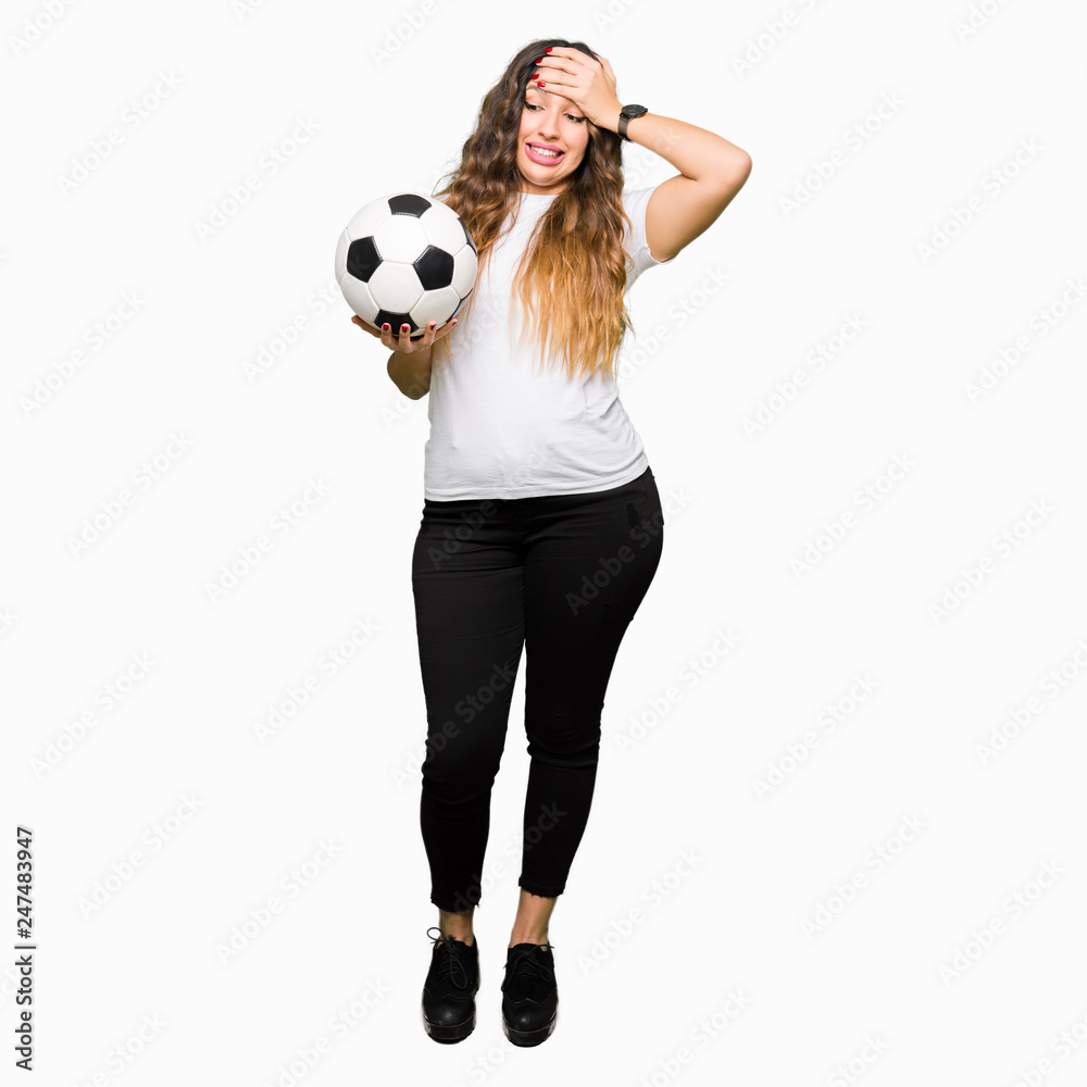 Young adult woman holding soccer football ball stressed with hand on head, shocked with shame and surprise face, angry and frustrated. Fear and upset for mistake.