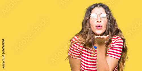 Young beautiful woman wearing glasses looking at the camera blowing a kiss with hand on air being lovely and sexy. Love expression.