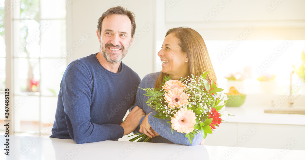 Romantic middle age couple holding flowers in love at home Romantic middle age couple holding flowers in love at home