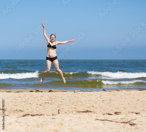 Happy young woman jumping on sea shore at sunny summer day