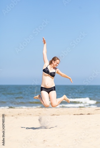 Happy young woman jumping on sea shore at sunny summer day