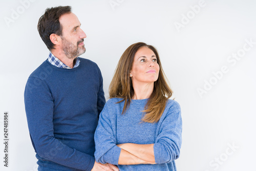 Beautiful middle age couple in love over isolated background smiling looking to the side with arms crossed convinced and confident