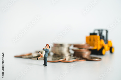Miniature people, husband and wife hug each other on stack coins and folklift truck background using as business success concept
