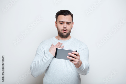 Shocked joy man playing video games on smartphone over white background.