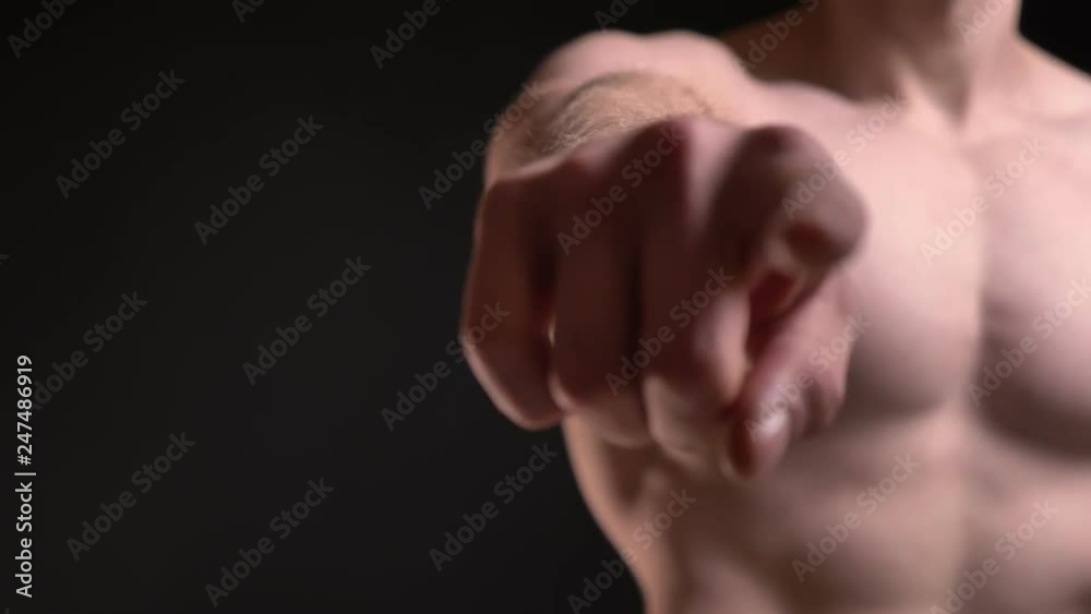 Close-up portrait of man with muscular biceps and breast pointing finger into camera on black background. Close-up portrait of man with muscular biceps and breast pointing finger into camera on black background.