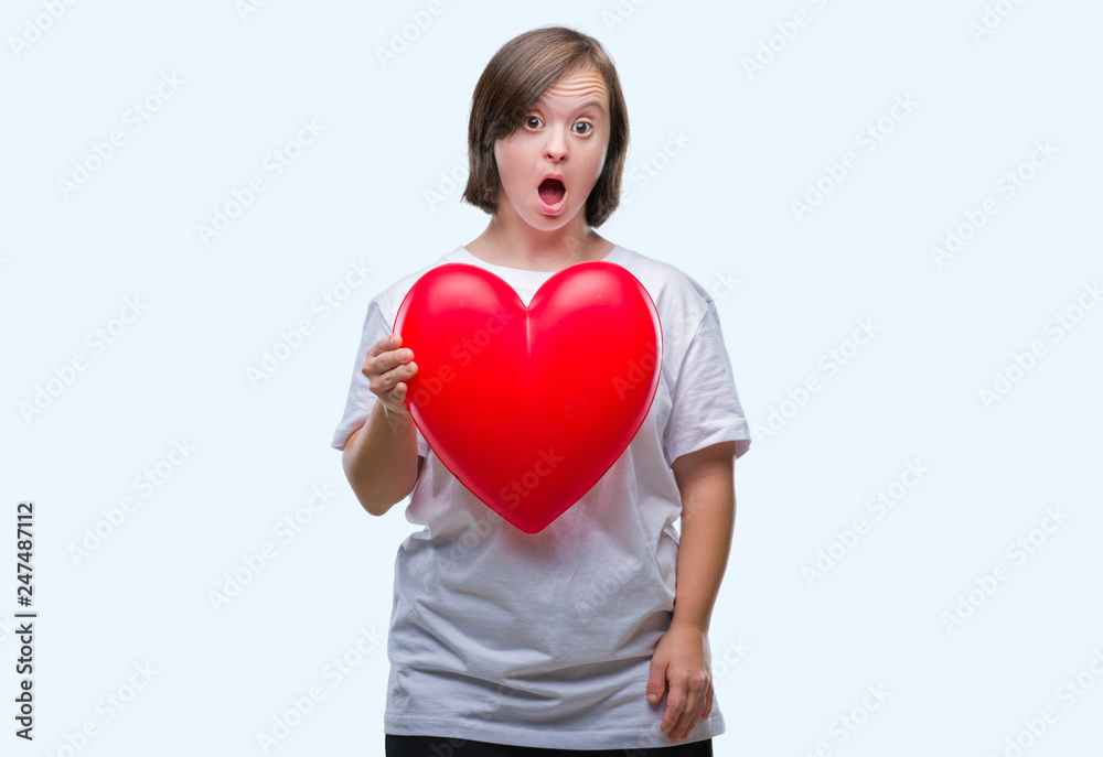 Young adult woman with down syndrome holding red heart over isolated background scared in shock with a surprise face, afraid and excited with fear expression Young adult woman with down syndrome holding red heart over isolated background scared in shock with a surprise face, afraid and excited with fear expression