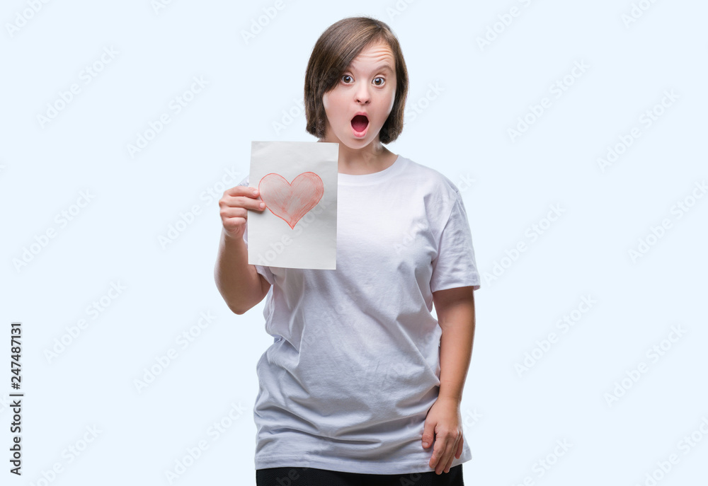 Young adult woman with down syndrome holding red heart card over isolated background scared in shock with a surprise face, afraid and excited with fear expression Young adult woman with down syndrome holding red heart card over isolated background scared in shock with a surprise face, afraid and excited with fear expression