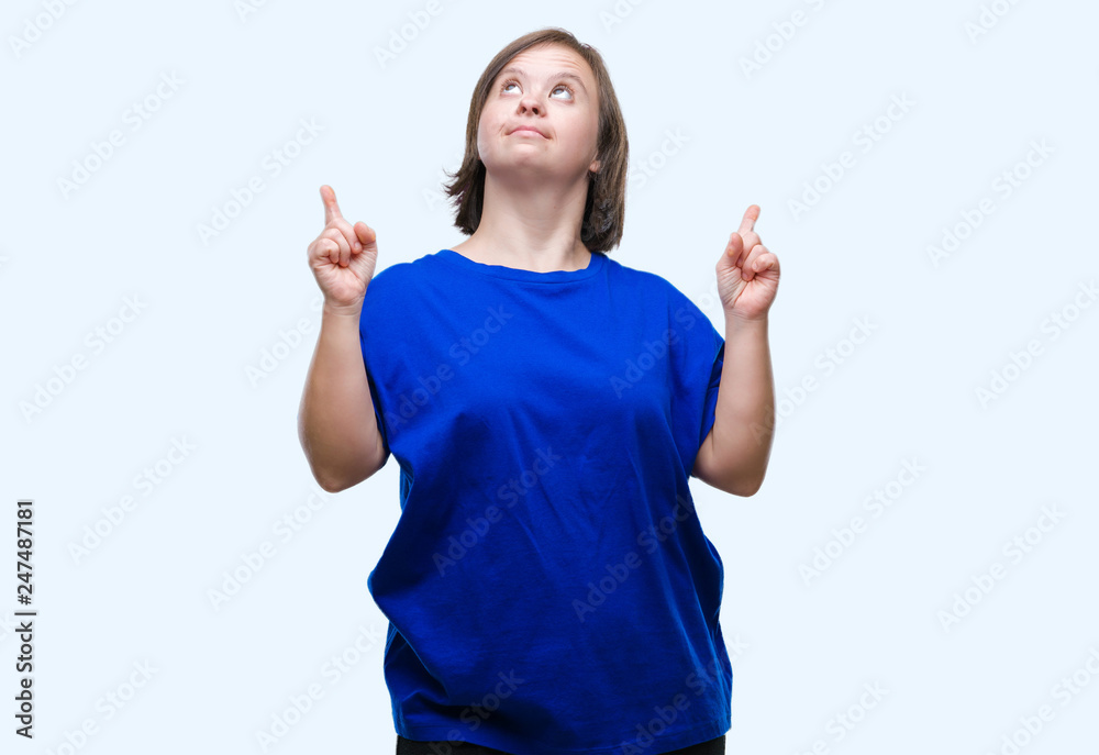 Young adult woman with down syndrome over isolated background amazed and surprised looking up and pointing with fingers and raised arms. Young adult woman with down syndrome over isolated background amazed and surprised looking up and pointing with fingers and raised arms.