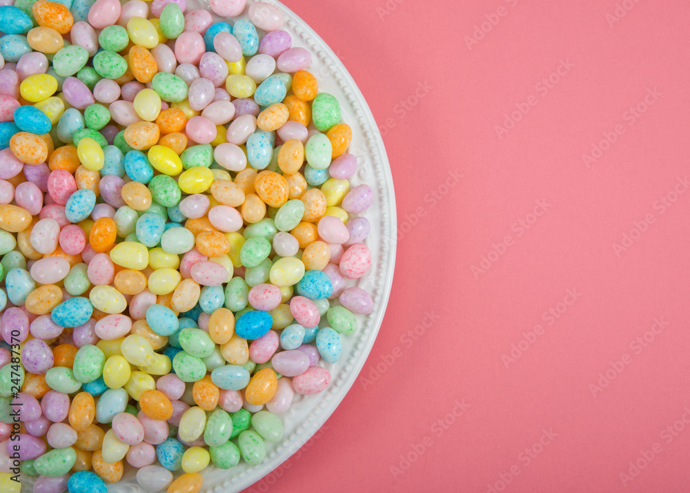 Many colorful candy jelly beans on porcelain plate laying on light pink surface with copy space. Popular Easter candy.