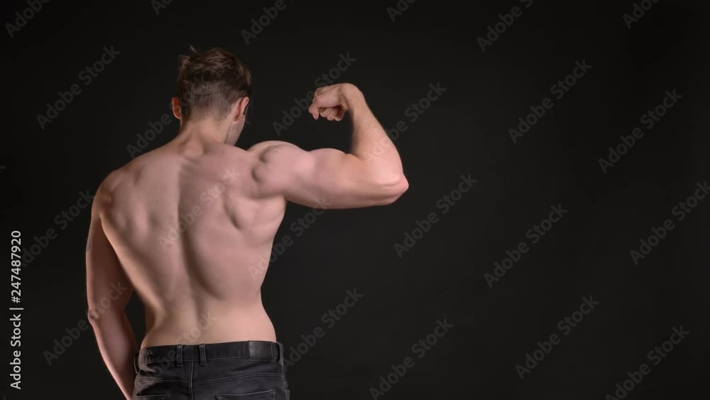 Rear portrait of young caucasian man showing his muscular biceps demonstrating his power on black background. Rear portrait of young caucasian man showing his muscular biceps demonstrating his power on black background.