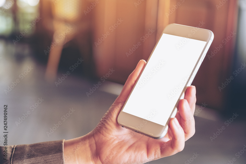 Mockup image of hand holding and using a white mobile phone with blank screen with blurred background in cafe Mockup image of hand holding and using a white mobile phone with blank screen with blurred background in cafe