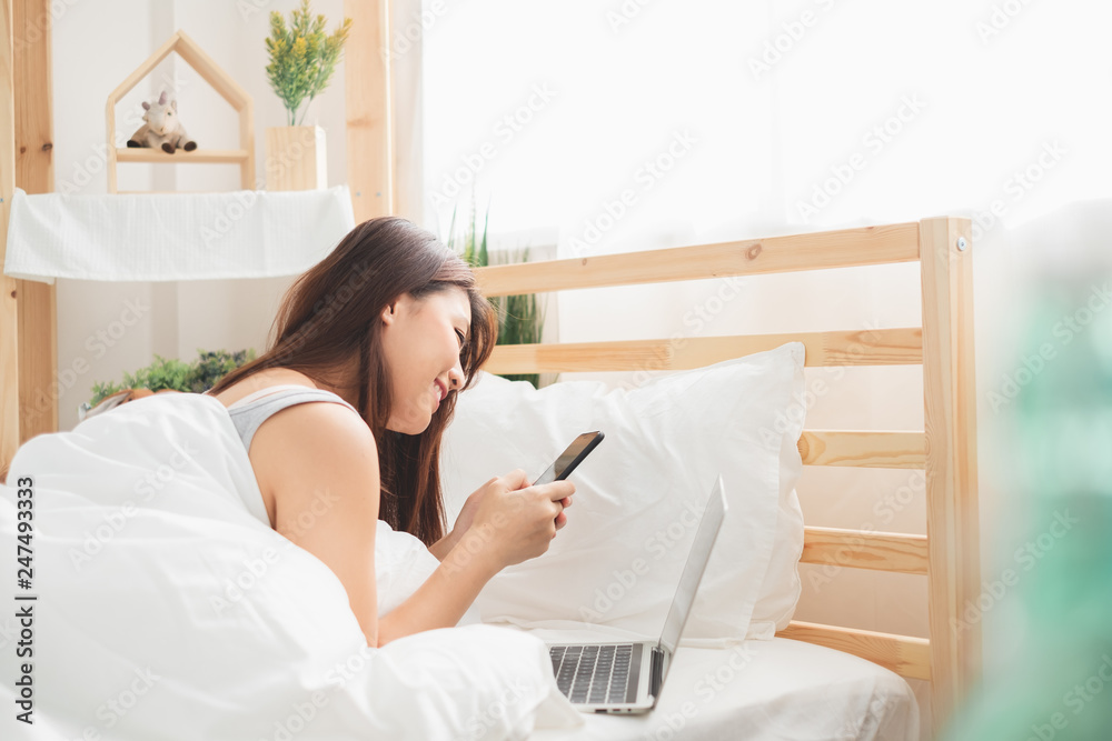 Beautiful Asian woman using laptop and smart phone in bed room for online shopping, Asian woman lifestyle concept Beautiful Asian woman using laptop and smart phone in bed room for online shopping, Asian woman lifestyle concept