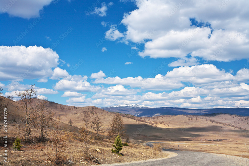 The road along the Tazheranskaya steppe to Lake Baikal. Spring landscape on the background of a beautiful sky with cumulus clouds