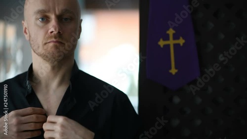 Young catholic priest dresses and buttons black shirt and a clerical colla