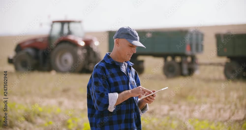 Farmer using digital tablet while examining field Farmer using digital tablet while examining field