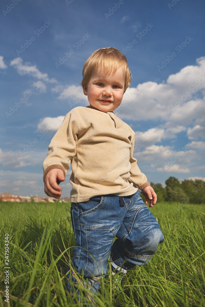 Happy childhood outdoor, little blond boy in green grass against the blue sky Happy childhood outdoor, little blond boy in green grass against the blue sky