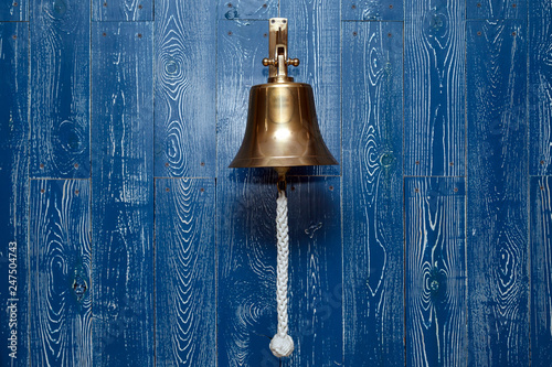 Copper old vintage bell, doorbell, rope on a wooden blue aged wall. Concept decor element in interior of deck, cabin of ship, restaurant, room, house decorated on marine theme photo