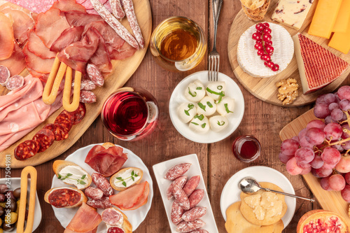 Charcuterie Tasting. Many different sausages and hams, deli meats, and a selection of cheeses, shot from above on a rustic background with glasses of wine, olives and grapes