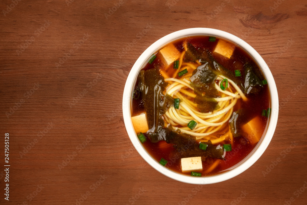 A bowl of miso shiru soup with tofu, scallions, noodles, and wakame seaweed, shot from the top on a rustic wooden background with copy space A bowl of miso shiru soup with tofu, scallions, noodles, and wakame seaweed, shot from the top on a rustic wooden background with copy space