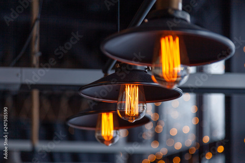 Black iron loft chandeliers with edison lamps on a black background, bokeh. Concept of modern interior design of restaurant, cafe, apartment, office, shop, wine bar © Тимур Конев