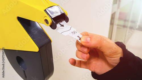 Customer pulls with hand a numbered ticket out of yellow number dispenser machine, to wait in service line and to be served when his number is displayed photo