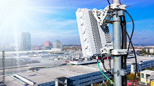 5G mobile telecommunication cellular radio network antenna on a mast on the roof broadcasting signal waves over the city on a clear sunny day with blue sky and clouds