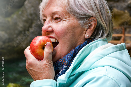 Healthy looking senior woman with grey hair eating apple outside in the park