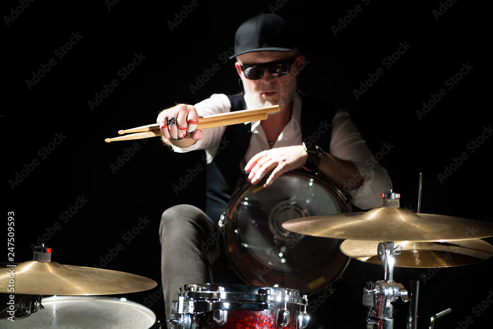 Fototapeta premium Drummer with a drumsticks in his hands sits behind drum kit on the black background