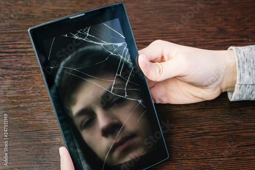 Reflection of the face of the teenager in the screen of the broken tablet. Teenage loneliness, depression. photo