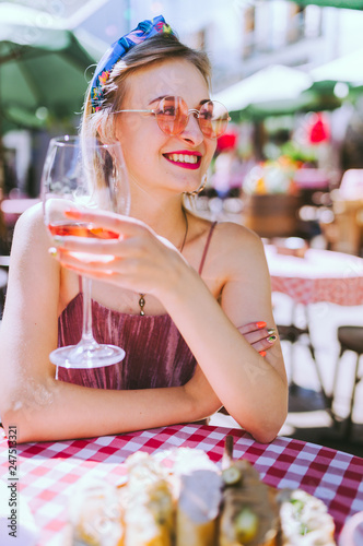 Beautiful woman with a headscarf on her head wearing pink sunglasses and resting in cafe with cocktail. Amazing blonde girl  with beautiful smile holding wineglass.