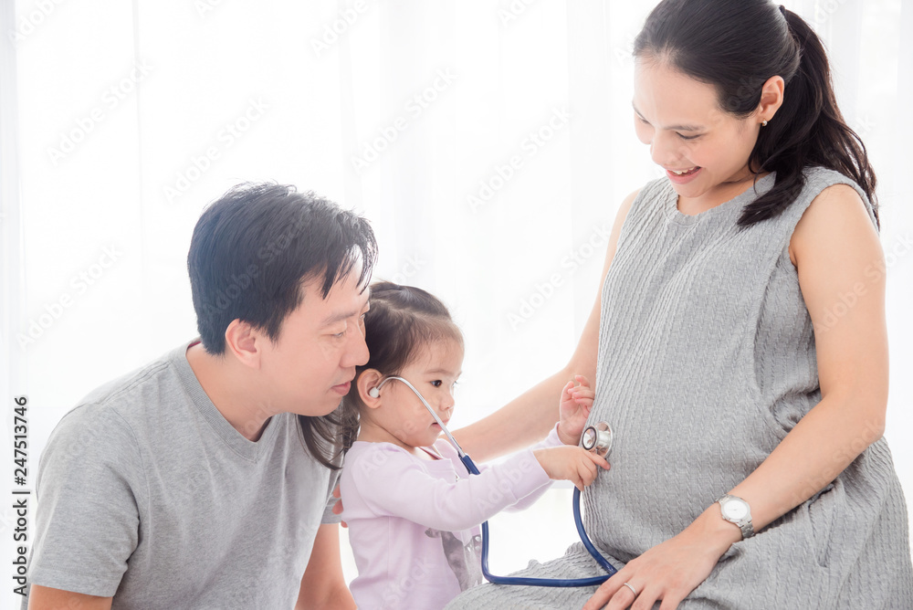 Little asian girl using stethoscope with her pregnant mother belly