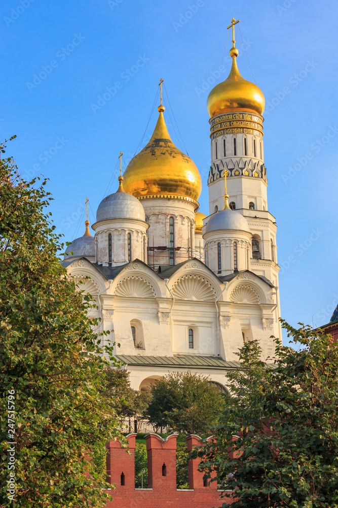 Cathedral of the Archangel and Ivan the Great Bell-Tower against Kremlin wall and green trees in sunny early morning