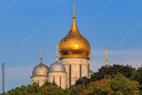 Cathedral of the Archangel on Moscow Kremlin territory on a blue sky and green trees background in sunny early morning