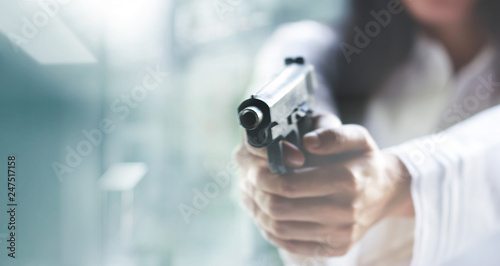 Woman pointing a gun at the target on blur background, criminal with gun, selective focus on front gun..