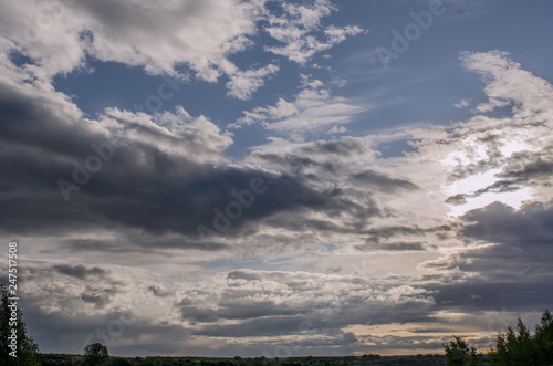 Cumulus clouds of fantastic shape soar in the sky in the sun's rays over the visible horizon line, toned.