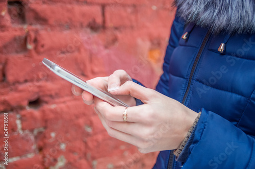 Girl pointing her finger at the screen of a smartphone on the background of a brick wall in an atmospheric city, using mobile phone text messages in female hands