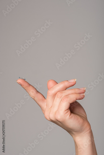 Soft contact lens on the finger of the female hand on a gray background