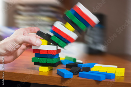 The hand dismantles the tower of multicolored wooden bars. Fall, destruction of an unstable tower. Concept: children's leisure, board games, instability, unstable situation.