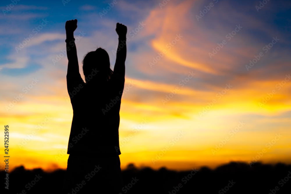 A happy young woman looks up at success and at sunset.