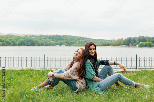 Smiling girls sitting back to back on grass