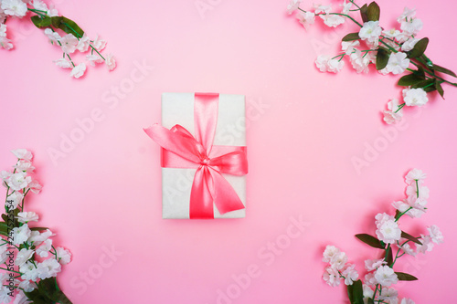Gift or present box and flower on pink table from above. Pastel color. Greeting card. Flat lay style.