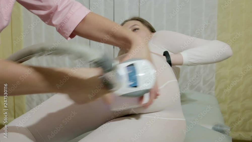 Sexy caucasian woman in white protective jumpsuit on LPG massage in beauty salon. The doctor moves the device on the slender body of the patient. Steadicam shot Sexy caucasian woman in white protective jumpsuit on LPG massage in beauty salon. The doctor moves the device on the slender body of the patient. Steadicam shot