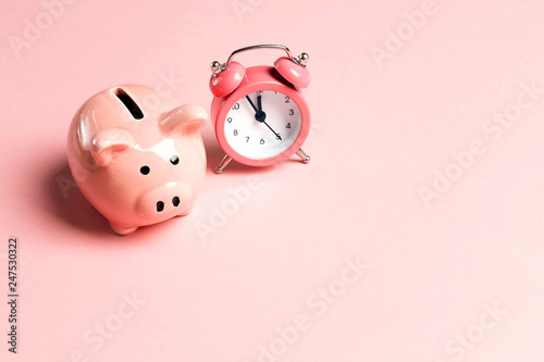 Piggy bank and classic alarm clock on pink background. Time to saving, money, banking concept.