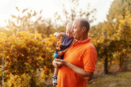 Grandfather holding his grandson while standing in vineyard at autumn. Grandson holding and eating grapes.