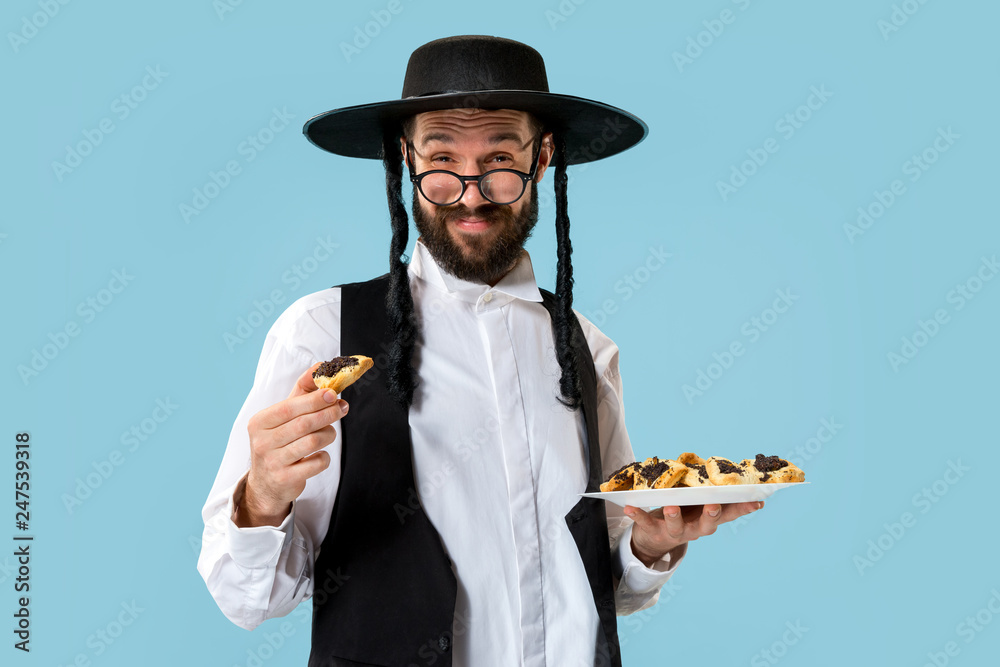 The young orthodox Jewish man with black hat with Hamantaschen cookies for Jewish festival of Purim at studio. The purim, jewish, festival, holiday, celebration, judaism, pastry, tradition, cookie The young orthodox Jewish man with black hat with Hamantaschen cookies for Jewish festival of Purim at studio. The purim, jewish, festival, holiday, celebration, judaism, pastry, tradition, cookie